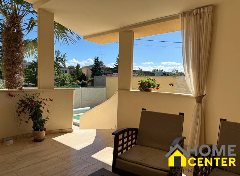 The terrace of a family house in Komárno with seating and a view of the yard with a palm tree.
