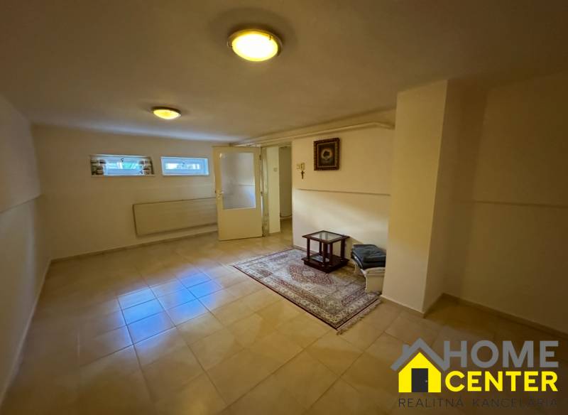 The interior of a family house with tiles, carpet, small windows, and a simple table.