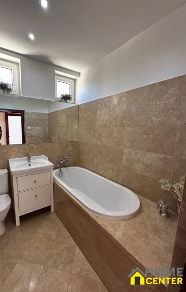 A bathroom in a family house with a bathtub, a sink, and brown tiles.