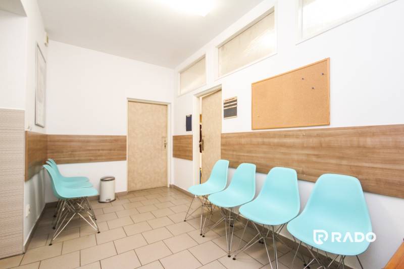 A waiting room with blue chairs, a cork bulletin board, and a wooden-patterned floor in an office.