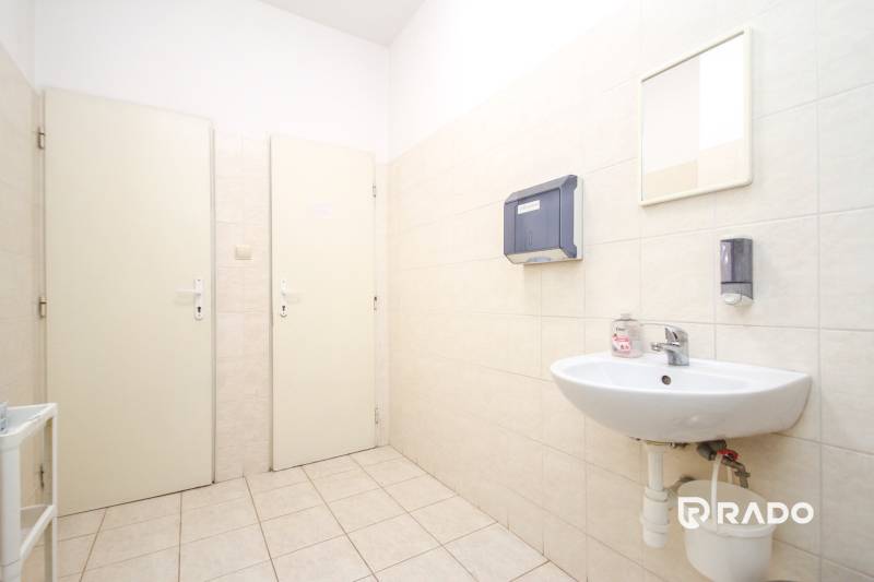 Office with a sink, dispensers, and a mirror. White tiles, light floor.