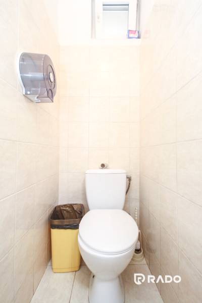 Toilet in the Office premises, light tiles, hanging holder and waste bin.