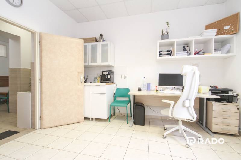 An office with a computer, a white chair, shelves, and a sink.