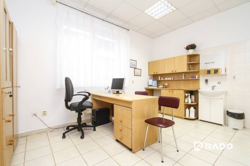 An office with a computer, desk, and chair, bright interior, shelves, and a sink.