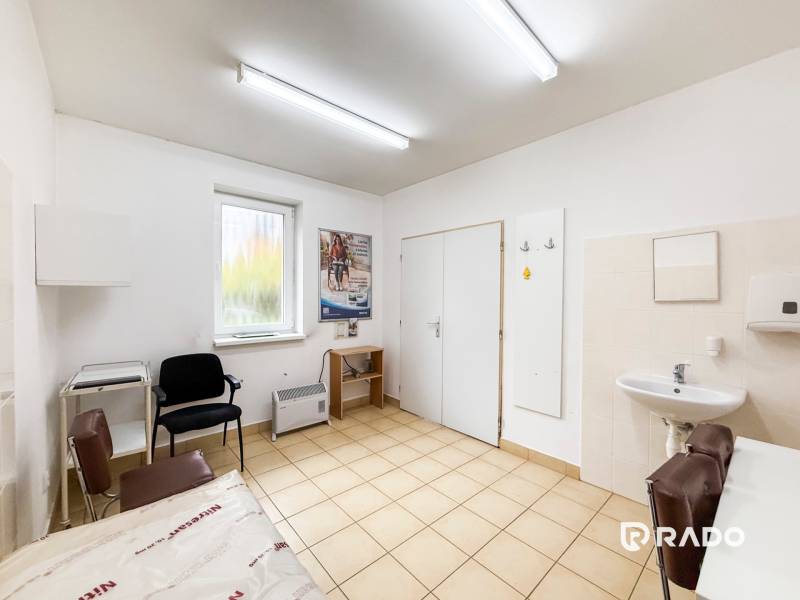 A doctor's office with a sink, chairs, and a window with a view, floor with a light decor.