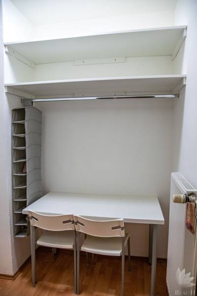 A workspace with a white desk, chairs, and storage shelves in a 2-room apartment.