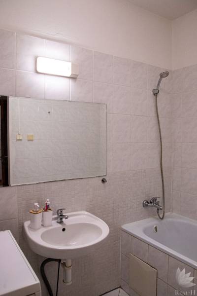 Bathroom in a 2-room apartment with a bathtub, sink, and lighting above the mirror.