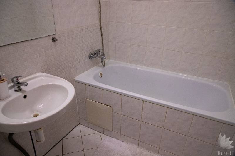 A bathroom with a bathtub, a sink, and tiles in a 2-room apartment.