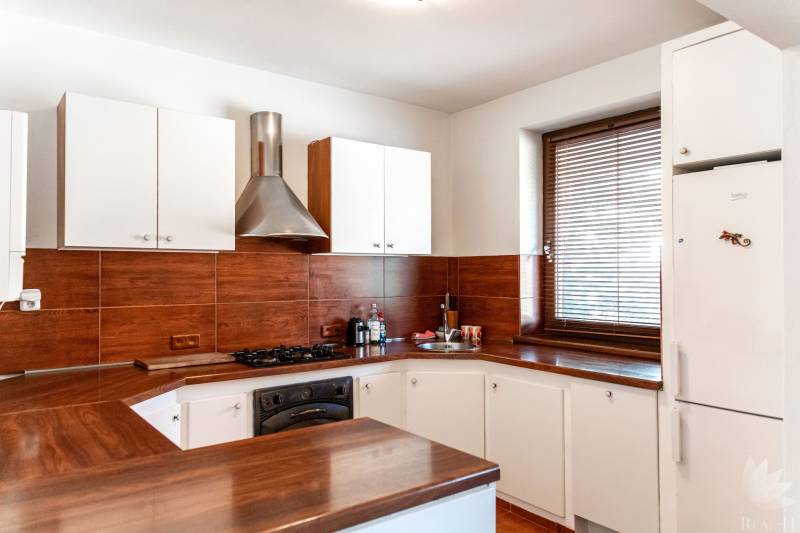A kitchen with white cabinets, brown tiles, and a dark workspace in a two-room apartment.