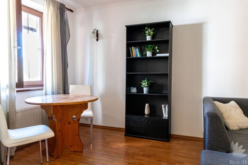 Living room with a window, table, bookshelf, two chairs, sofa, and wooden-patterned floor.
