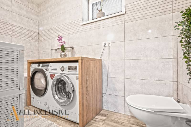 A bathroom in a 3-room apartment with a washing machine, dryer, and a floor with a wooden decor.