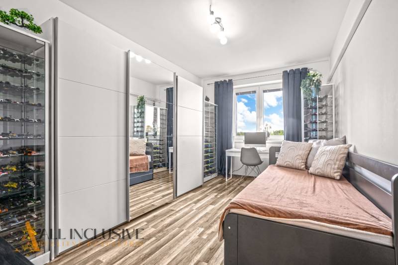 A room with a mirrored wardrobe, a desk, and a floor with a wooden decor in a 3-room apartment.