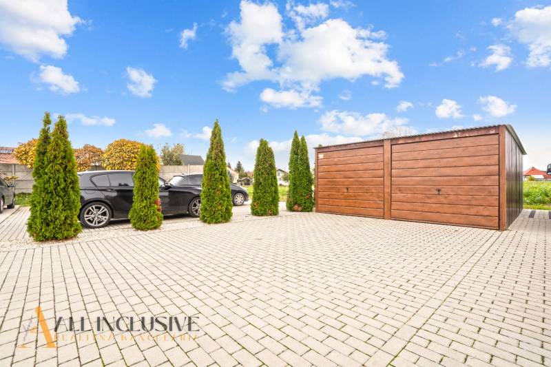 Parking lot by a 3-room apartment in Gabčíkovo, with cars and a wooden garage.