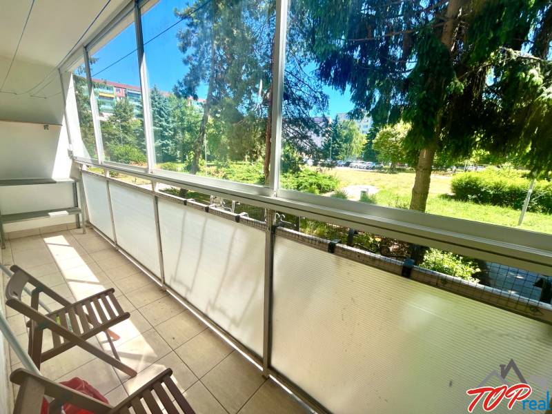 Glazed loggia with wooden chairs and a view of greenery in a 3-room apartment.