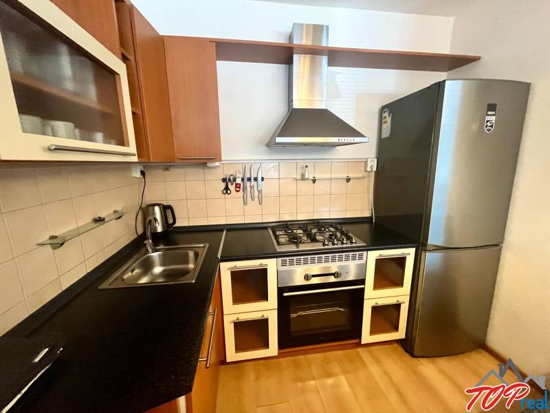 A kitchen in a 3-room apartment with a gas stove, a range hood, and a modern refrigerator.