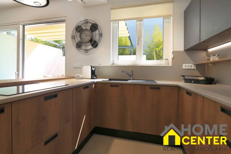 A kitchen in a villa with a large window, wooden cabinets, and a wooden decor floor.