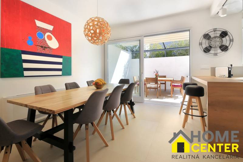 Bright dining room in the villa with a wooden table, colorful painting, and terrace.