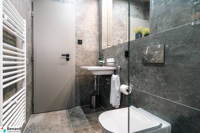 Bathroom in a 2-room apartment with dark tiles, sanitary ware, and a mirror.
