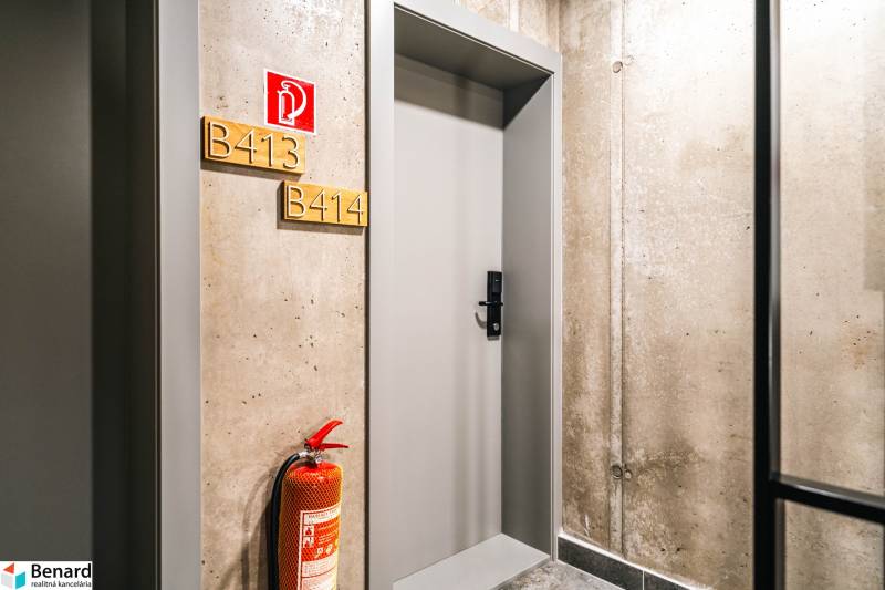 Concrete hallway with doors to a 2-room apartment and a fire extinguisher.