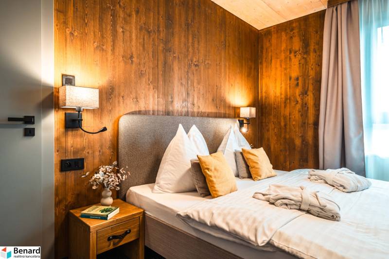 A bedroom with wooden paneling, a comfortable bed, and a side table in a two-room apartment.