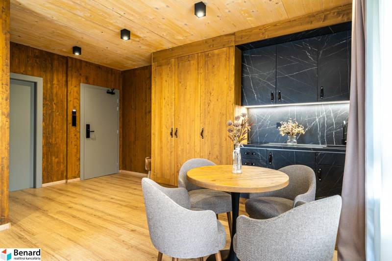 Interior of a 2-room apartment with wood-patterned flooring, wooden walls, and a black kitchen unit.
