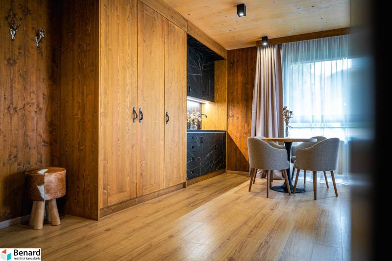 A room in a 2-room apartment with a kitchenette, wooden walls, and a floor with a wood decor.