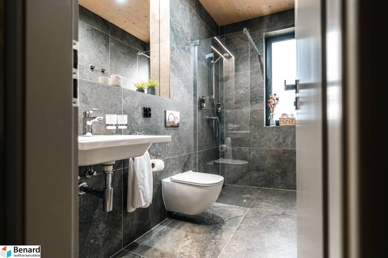 A bathroom with a shower and large gray tiles in a 2-room apartment.