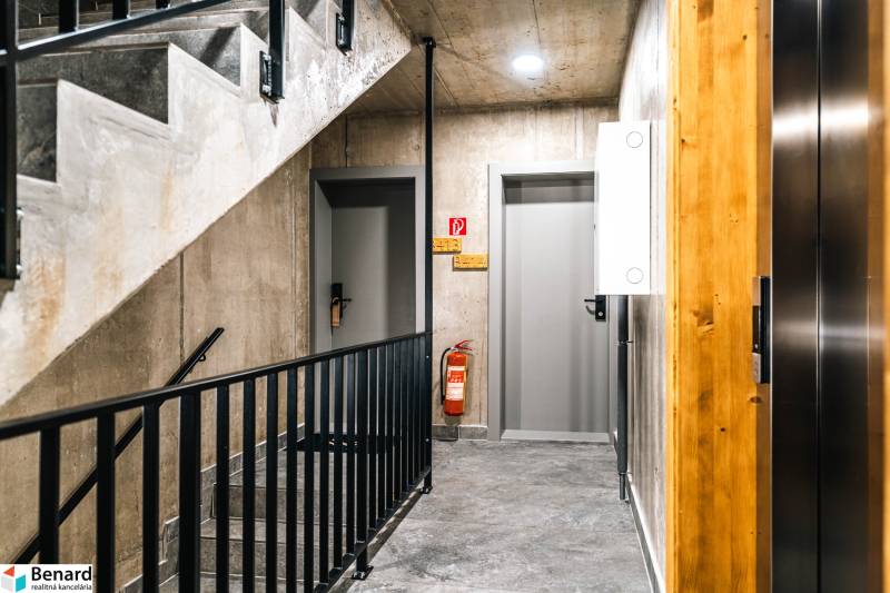 A hallway with concrete walls and metal railing in a 2-room apartment, with modern lighting.