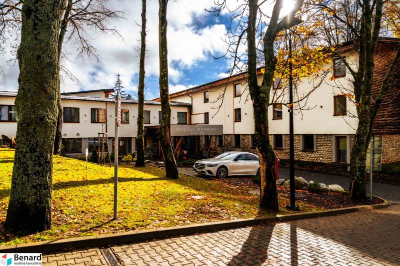 The hotel building in Štrba on Lúčná surrounded by trees, with a parked car.