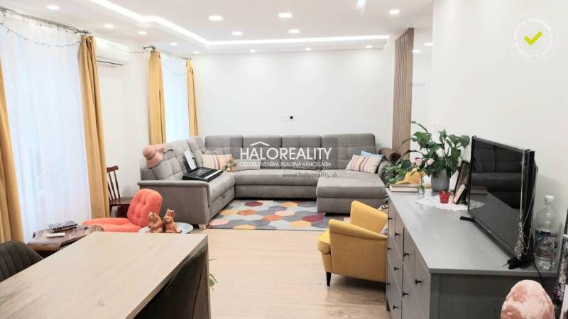 A living room in a three-room apartment with a wooden decor floor, a gray sofa, and a yellow armchair.
