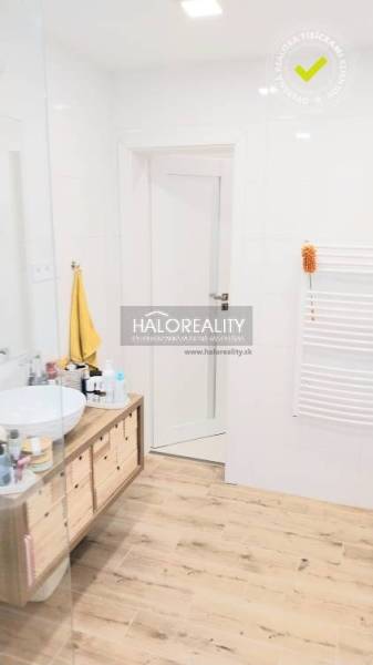 A bathroom with a wooden decor floor, a countertop sink, and white walls in a three-room apartment.