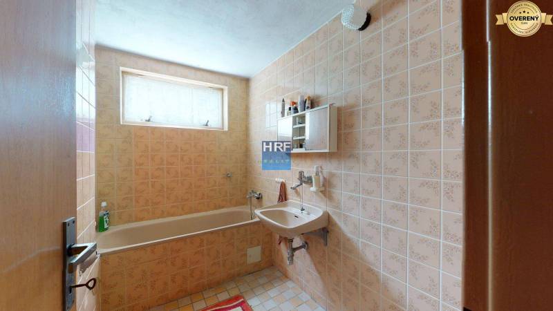 A bathroom in a family house with older tiles, a bathtub, and a sink.