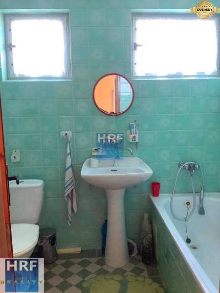A bathroom in a family house with turquoise tiles, a sink, a mirror, and a bathtub.