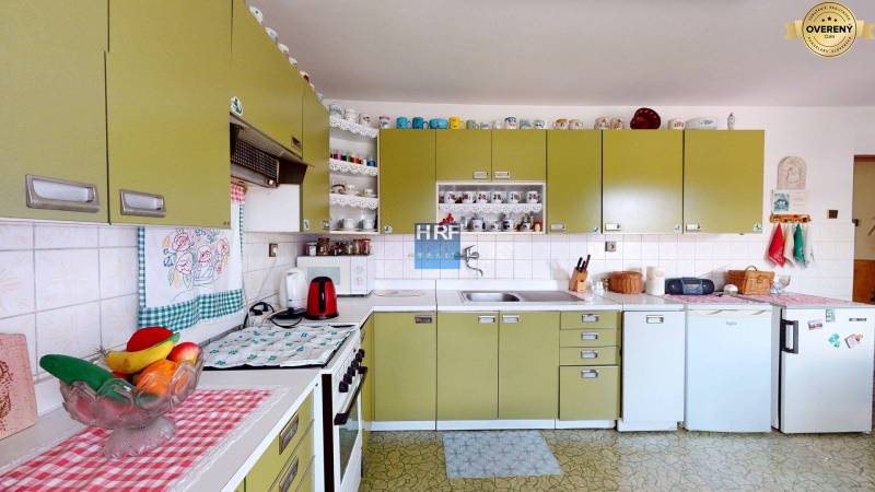A kitchen in a family house with olive cabinets, appliances, and shelves with cups.