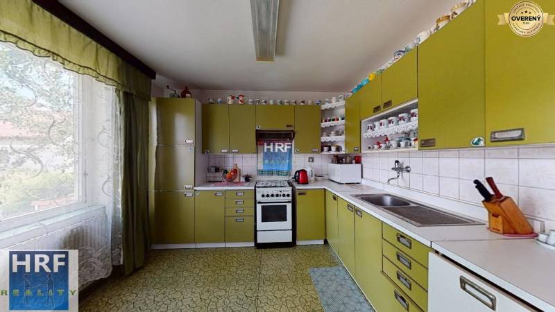 A kitchen in a family house with olive cabinets, ceramic tiles, and many cups on the shelves.