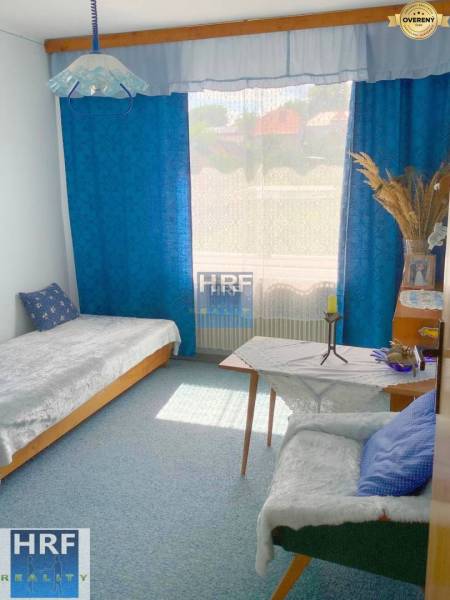 A room in a family house with blue curtains, a sofa, and a bed.