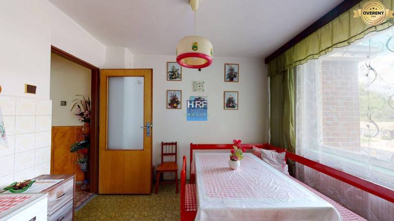 Dining room in a family house with a table, curtains, and floral paintings on the wall.