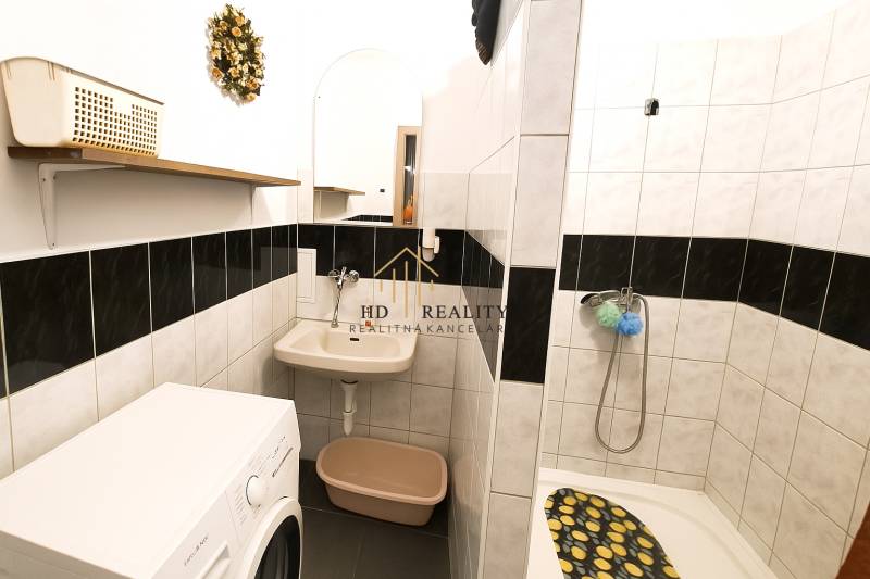 Bathroom with a washing machine, shower, and sink in a 2-room apartment.
