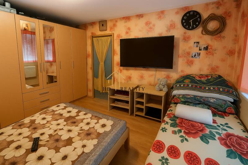 A bedroom with floral wallpaper, a wardrobe, a bed, and a wooden decor floor in a two-room apartment.