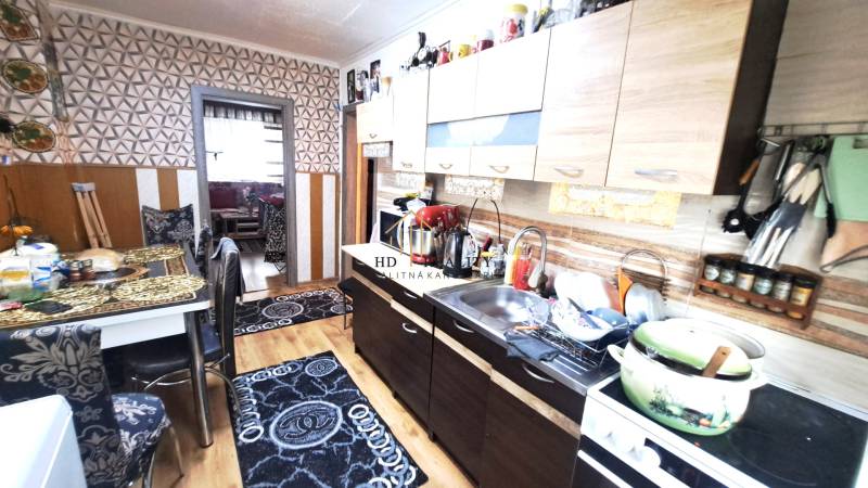 A kitchen in a 2-room apartment with a wooden decor floor and geometric wallpaper.