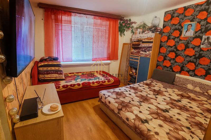 A bedroom in a two-room apartment with a wooden decor floor and colorful bed linens.