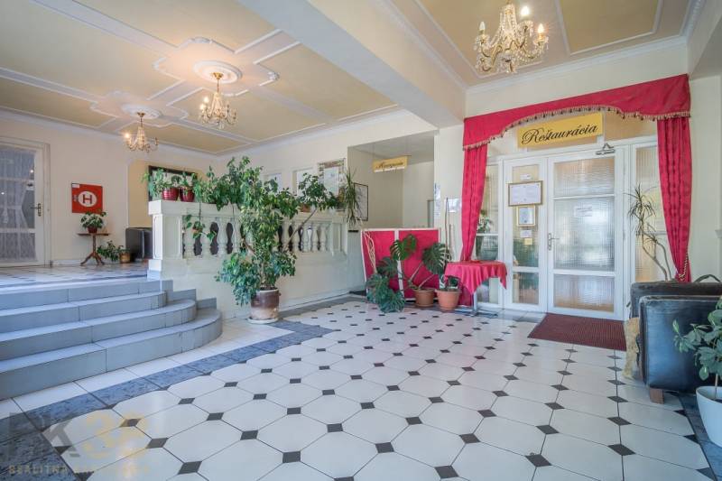 Hotel reception with plants and chandeliers, geometric patterned tiles.