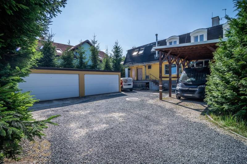 A parking lot in front of the guesthouse with garages in Poprad surrounded by coniferous trees.