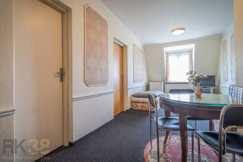 Interior of a hotel and guesthouse with a round table, carpet, TV, and decorative walls.