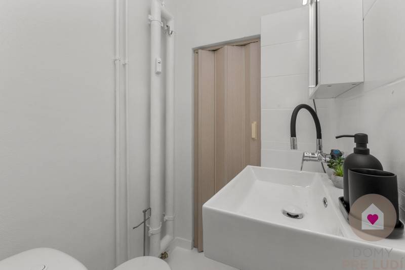 Compact bathroom in a studio apartment with a sink, faucet, and sliding doors.