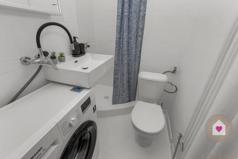 A bathroom in a studio apartment with a washing machine, sink, and toilet.