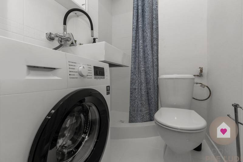 Compact bathroom in a studio apartment with a shower, washing machine, and toilet.
