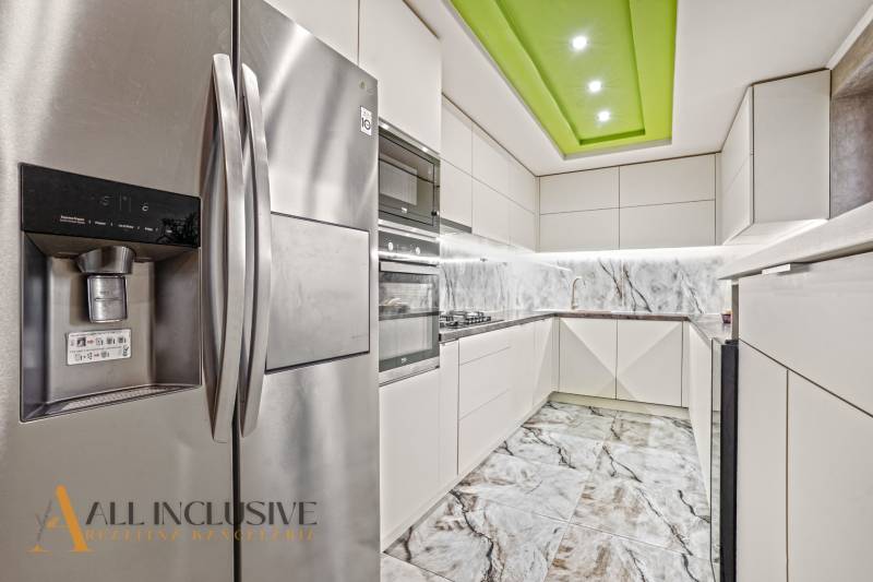 A kitchen in a family house with white cabinets, a marble backsplash, and a stainless steel refrigerator.