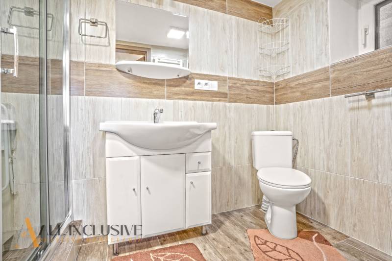 A bathroom in a family house with a sink, shower, and a floor with a wooden decor.
