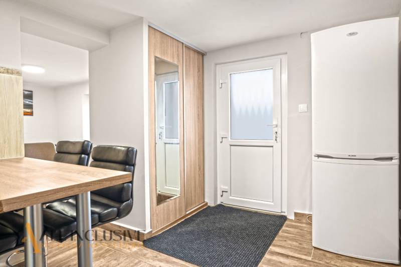 Entrance area in a family house with a refrigerator, mirror, chairs, and a wooden-patterned floor.